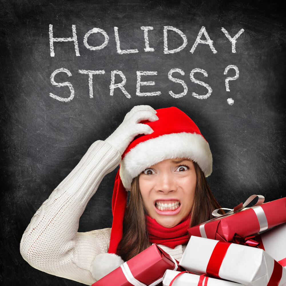 Stressed woman shopping for gifts holding Christmas presents wearing red Santa hat looking angry and distressed with funny expression on black chalkboard background.
